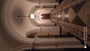 A grand, symmetrical hallway with a checkered floor and white walls, leading to a central light fixture. - Double B Ferruccio I (Rome)