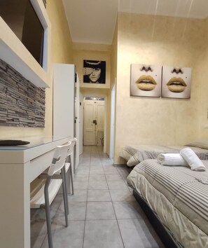 Une chambre d’hôtel étroite, avec un bureau, des chaises, un lit avec une literie à rayures et deux tableaux représentant des lèvres, accrochés au mur.