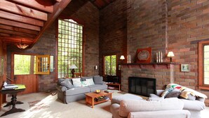 A cozy living room with a fireplace, large windows, and a comfortable seating area. - River's Bend (Saugatuck)