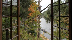 A view through a window of a river with a dock, surrounded by trees and a wooden bridge. - River's Bend (Saugatuck)