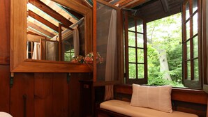 A wooden cabin interior with a bench, a window with a view of greenery, and a mirror reflecting the room. - River's Bend (Saugatuck)