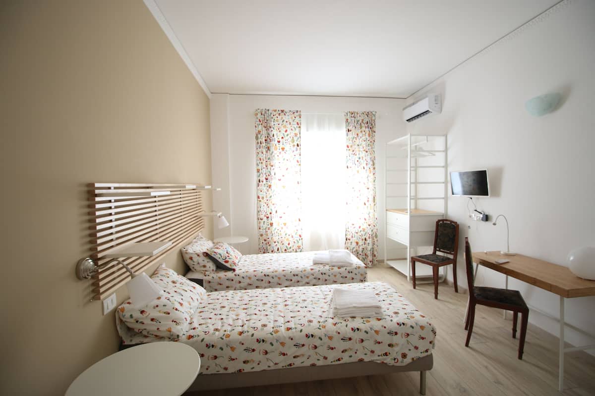 A hotel room with two beds, a desk, a chair, a TV, and a window with curtains.