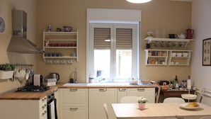 Een keuken met witte kasten, een fornuis, een spoelbak en een raam met jaloezieën.