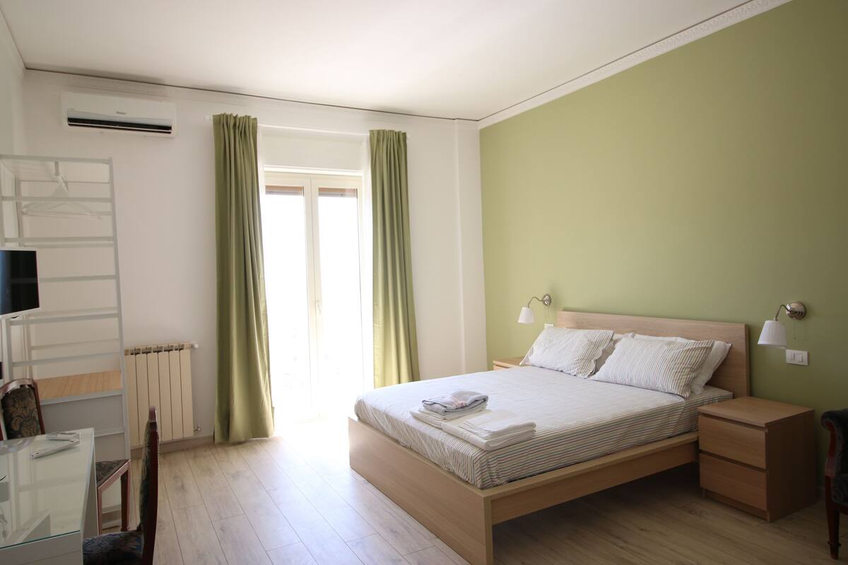 A bedroom with a wooden bed, bedside tables, a desk, and a chair.