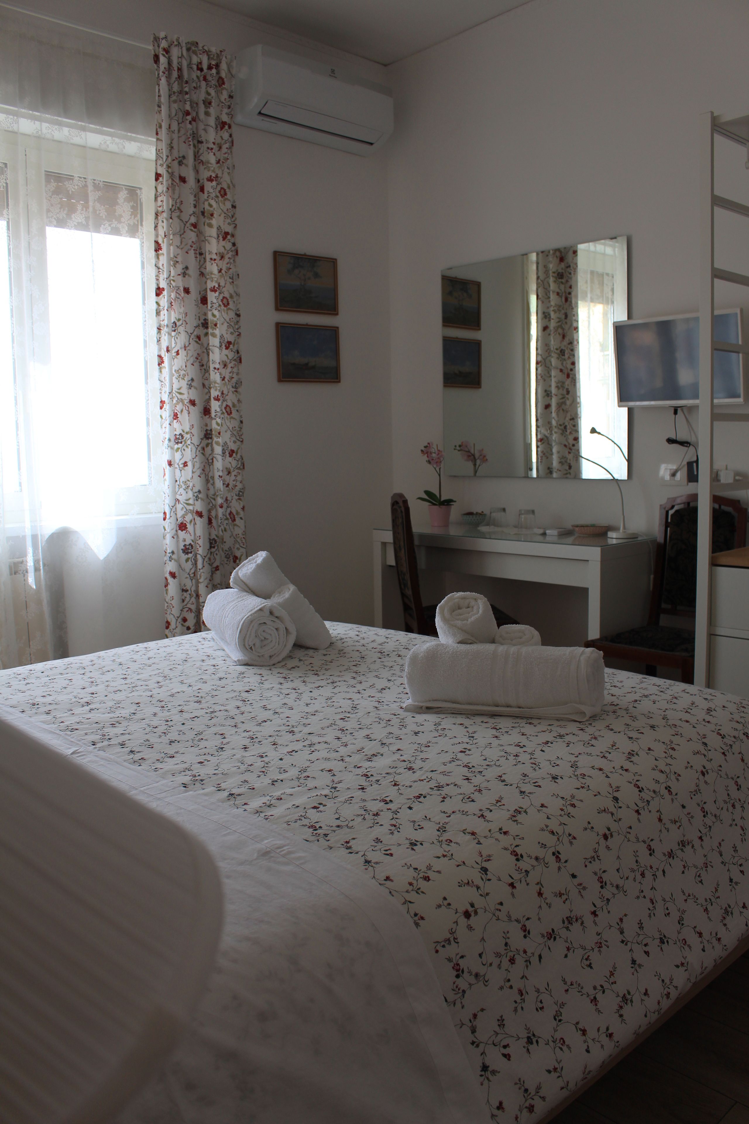 A hotel room with a bed, a desk, a chair, a mirror, and a potted plant.