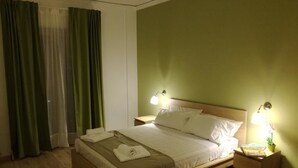 Een hotelkamer met een bed, twee bedlampen, een nachtkastje en een raam met gordijnen.