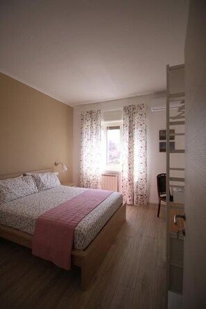 A bedroom with a bed, a chair, a radiator, and a window with curtains. - L'Alba sui Templi - Bed & Breakfast (Agrigento)