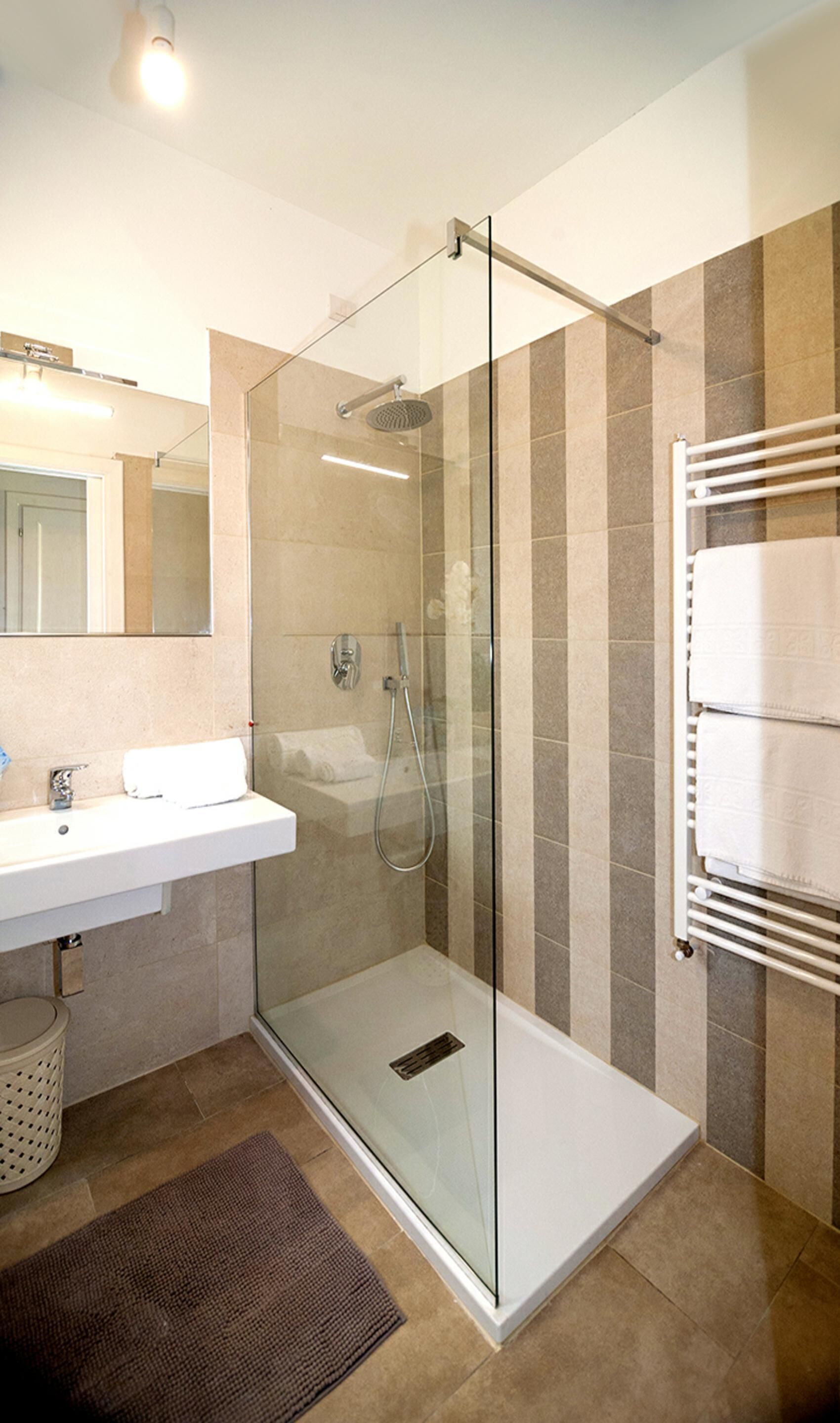 Un baño moderno con ducha envuelta en vidrio, un lavamanos blanco y un perchero para toallas.