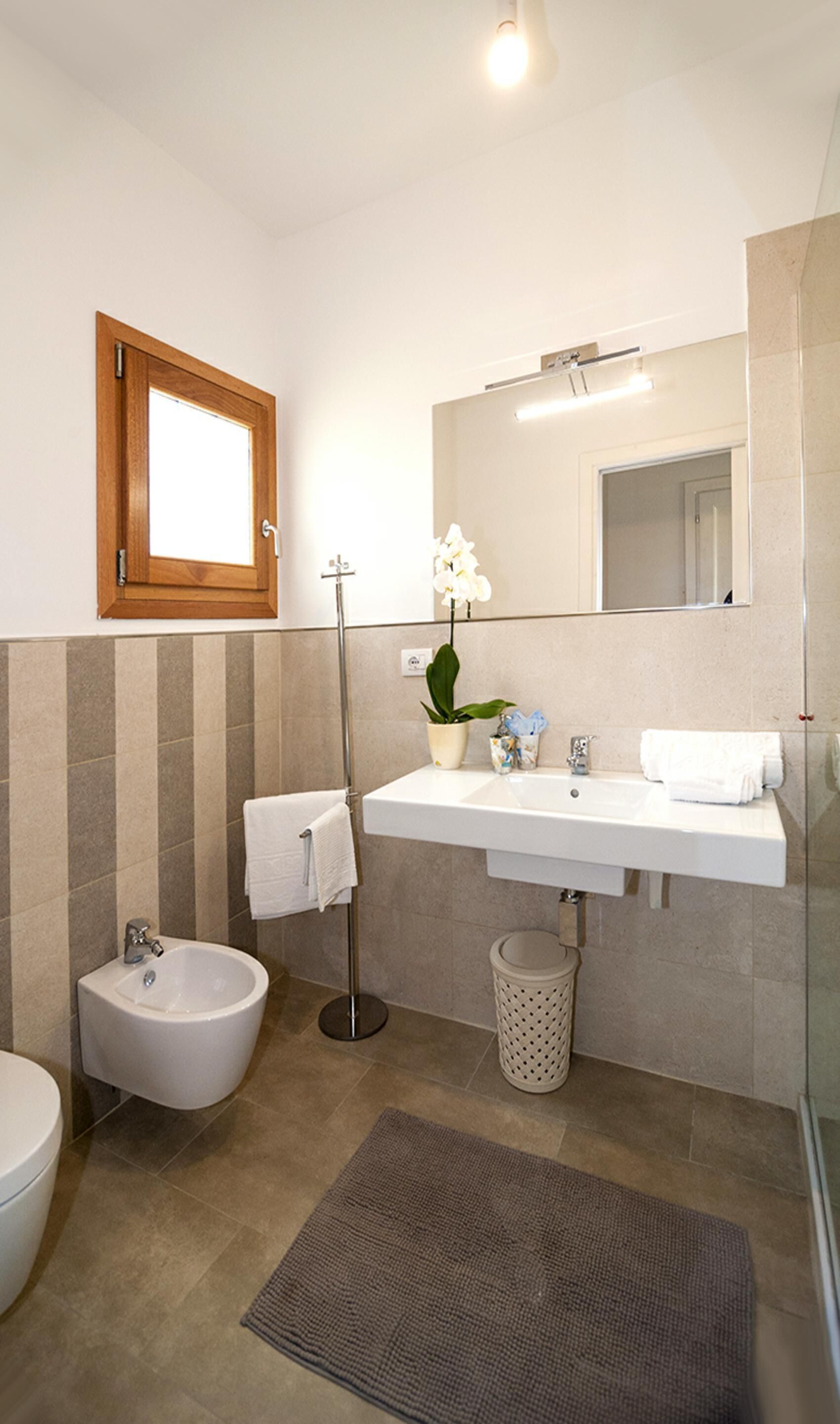 A modern bathroom with a bidet, a sink with a mirror above, and a potted orchid.
