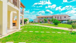 A residential area with a well-maintained lawn, paved pathways, and a row of houses with balconies and a tiled roof. - Stella Marina Camere sul mare (Budoni)