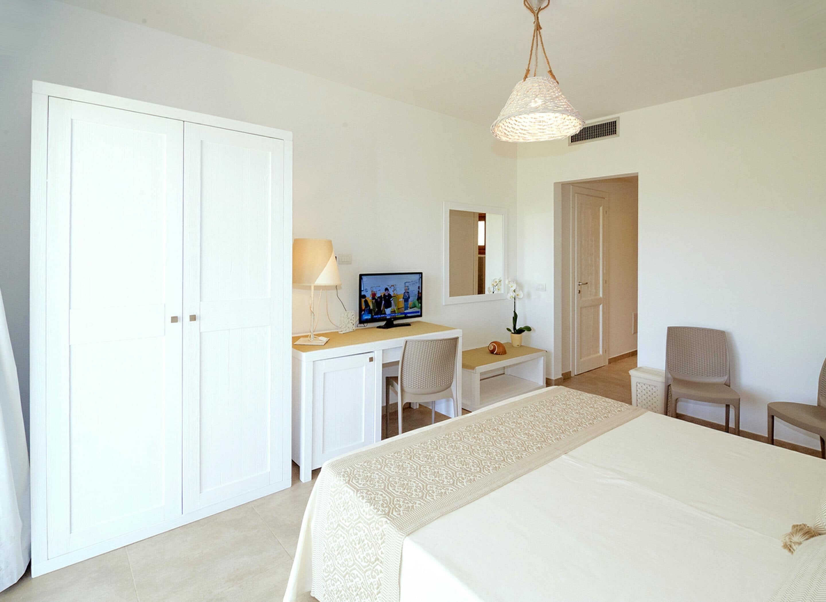 A hotel room with a bed, a desk with a computer, a chair, a television, and a wardrobe.
