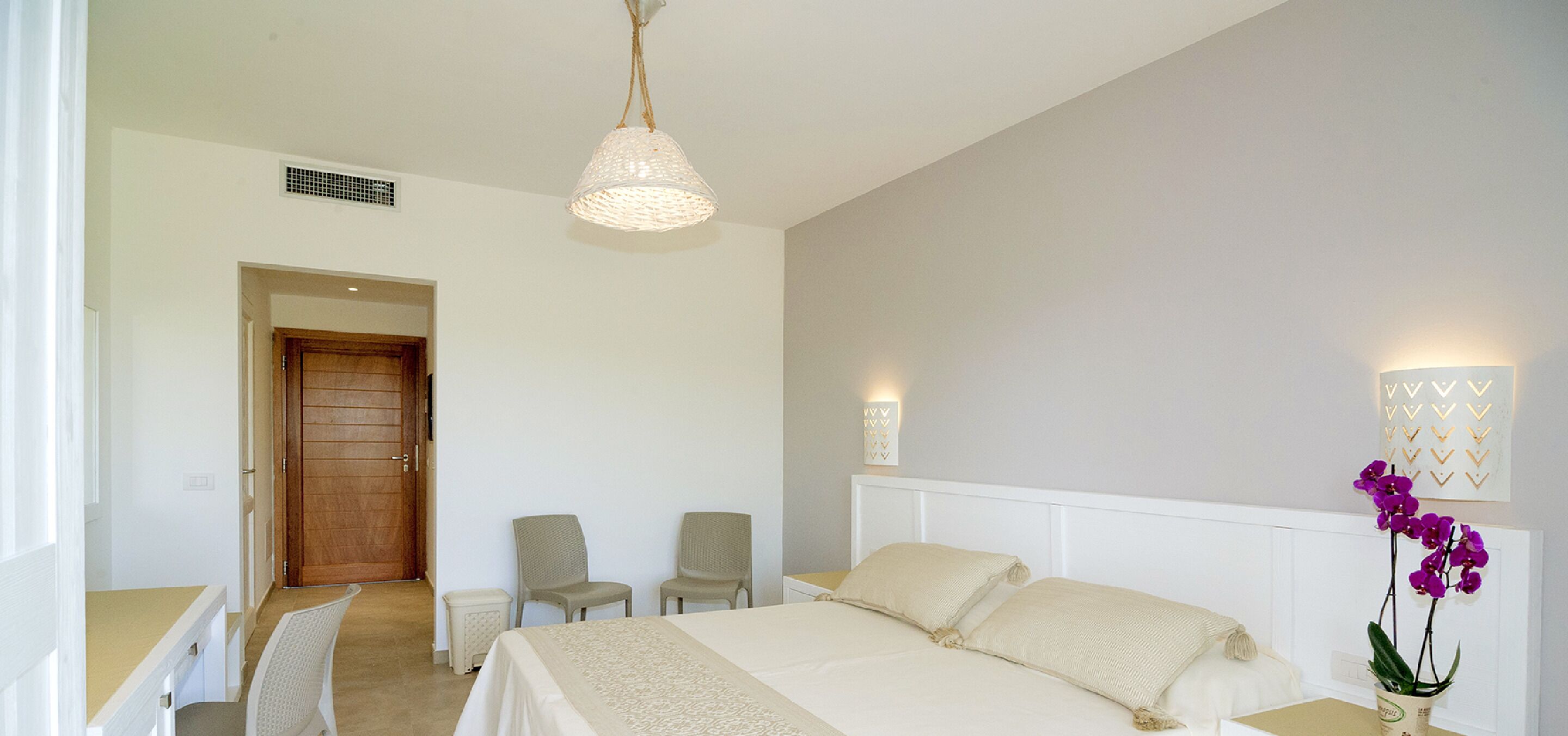 Ein Schlafzimmer mit einem Bett, zwei Stühlen, einem Nachttisch, einer Lampe und einer Wandleuchte.