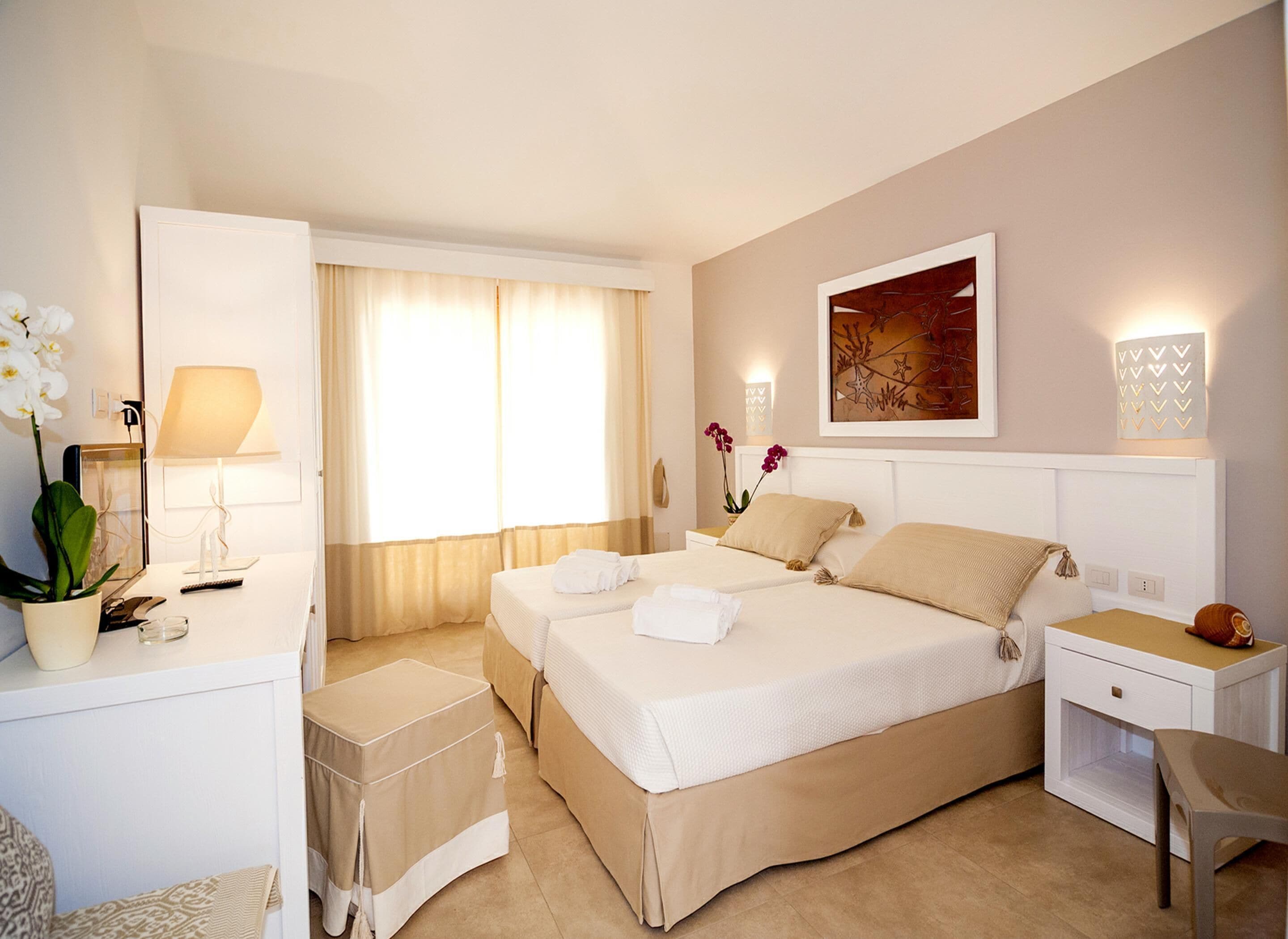 A hotel room with two beds, a desk with a lamp, a chair, and a small table.