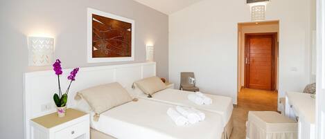 A hotel room with a large bed, two bedside tables, a nightstand, a chair, a small table, and a door.