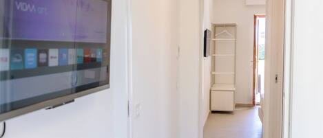 A hallway with a flat-screen TV mounted on the wall, a white door, and a tiled floor.