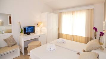 A hotel room with two beds, a desk with a computer, a chair, and a small table with a lamp.