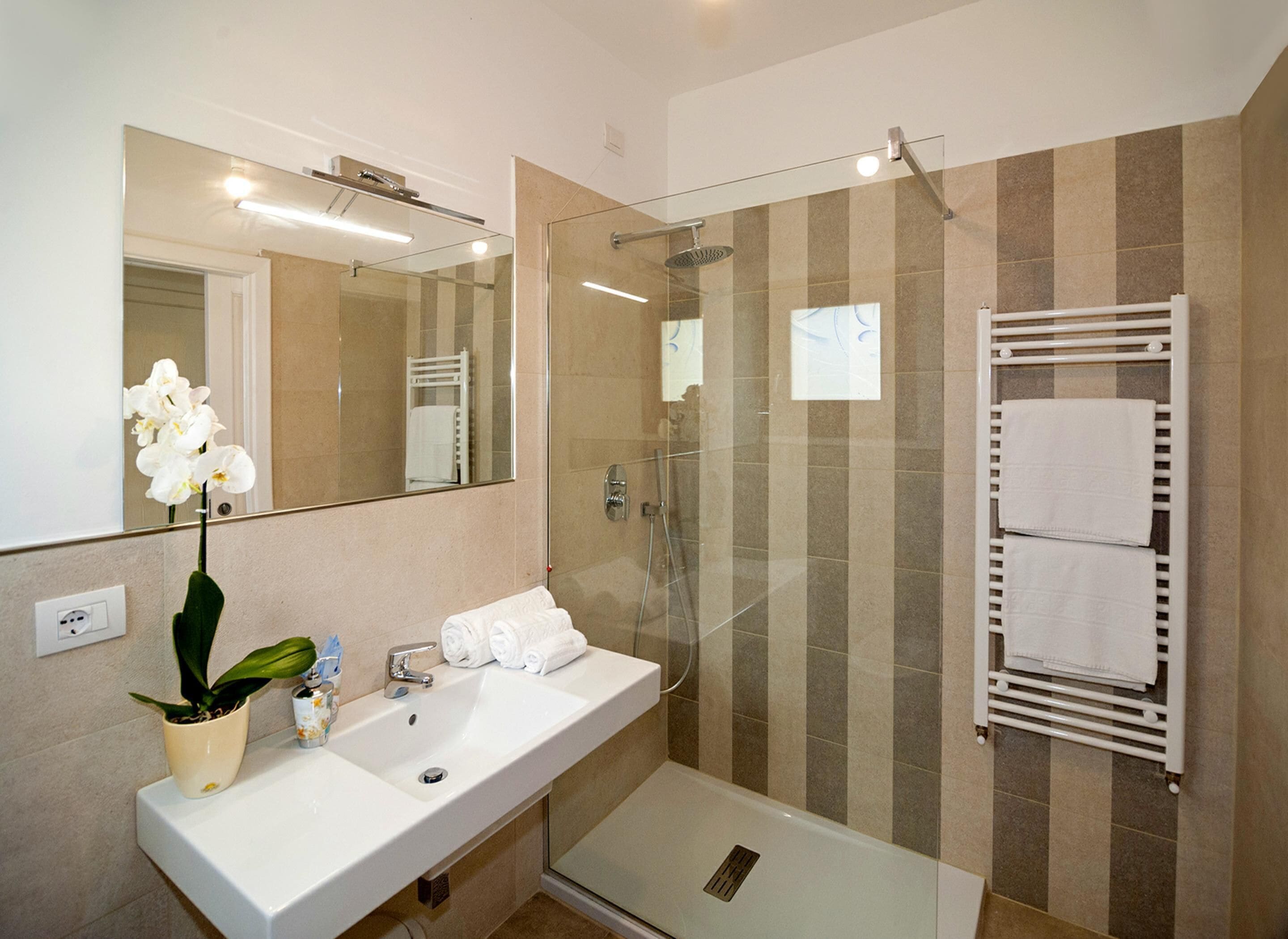 A modern bathroom with a glass-enclosed shower, a white sink, and a towel rack.