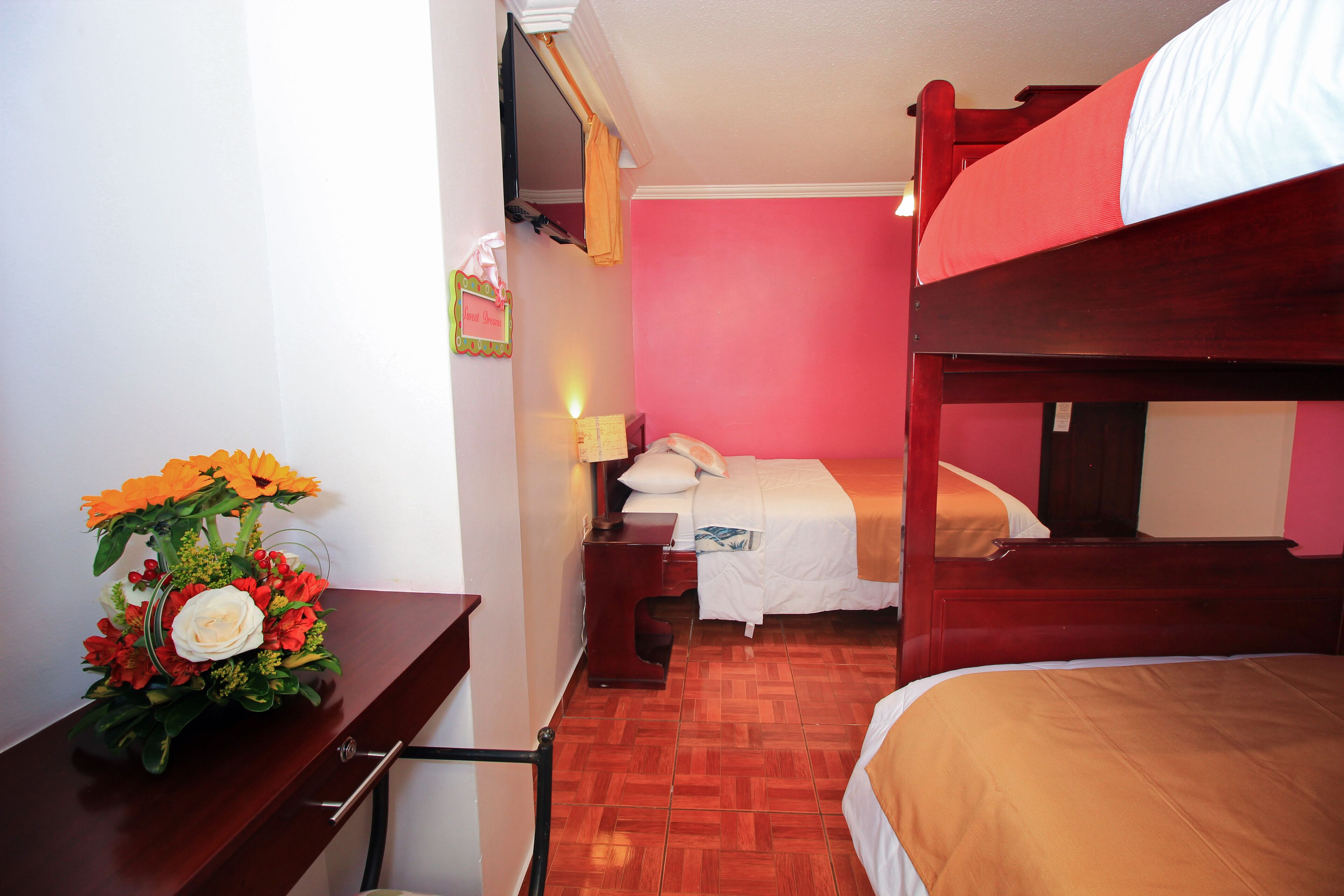 A room with a bunk bed, a desk with a flower arrangement, and a nightstand with a lamp.