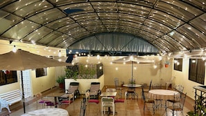 Un patio interior con varias mesas y sillas, techo curvo y luces colgantes.