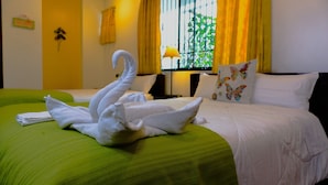 Habitación de hotel con colcha verde, toallas blancas y una escultura decorativa de cisne hecha con toallas.