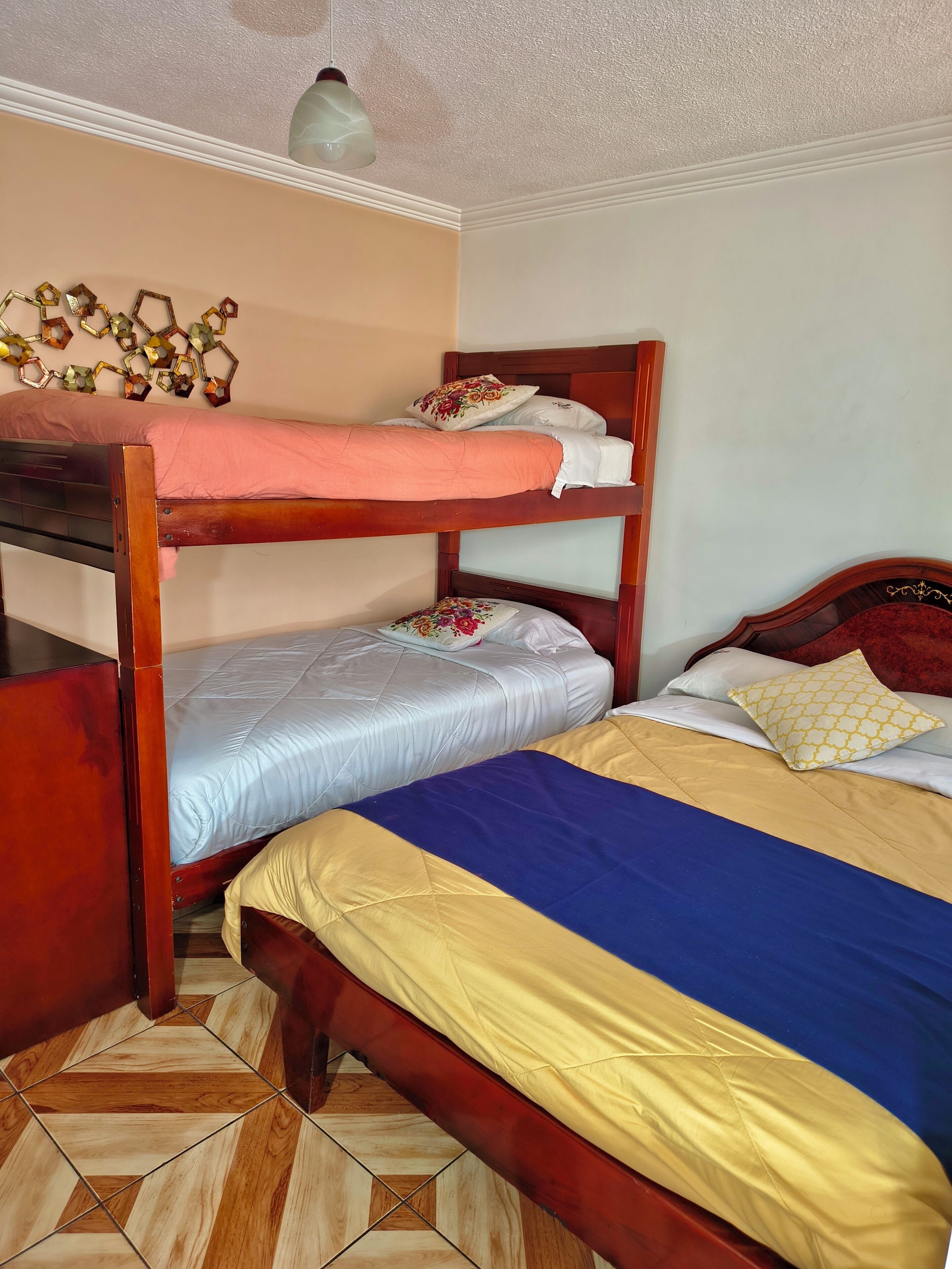 A bunk bed with a wooden frame, a lower bed with a blue and yellow bedspread, and a decorative wall piece above the beds.