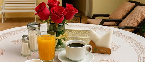 A breakfast table with pancakes, scrambled eggs, orange juice, coffee, and red roses.