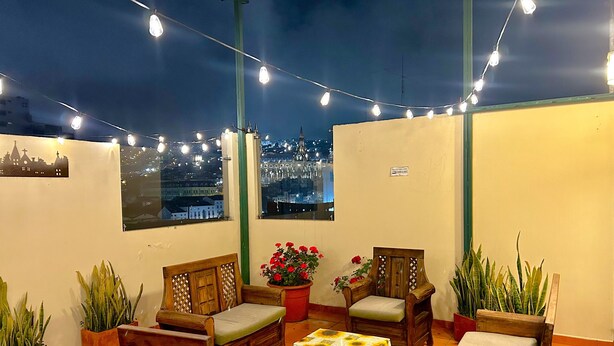 Una terraza en la azotea con muebles de madera, plantas en macetas y guirnaldas de luces.