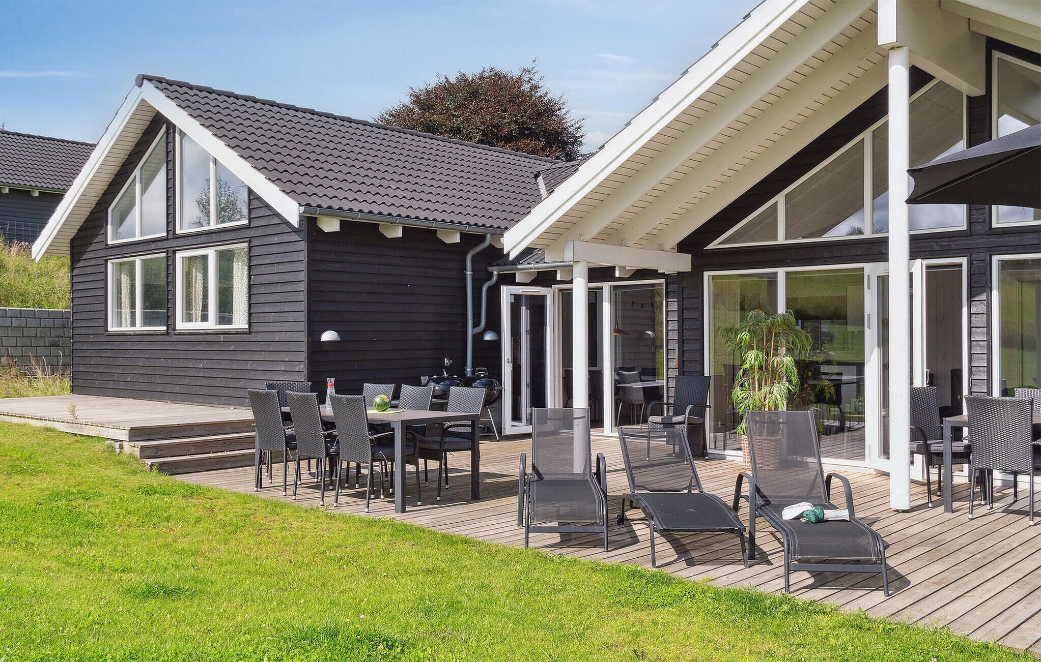 Een modern huis met een terras, straffen buitenmeubels en een glazen deur naar een overdekte ruimte.
