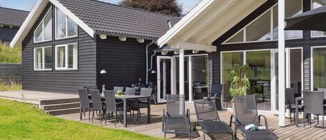 Een modern huis met een terras, straffen buitenmeubels en een glazen deur naar een overdekte ruimte.
