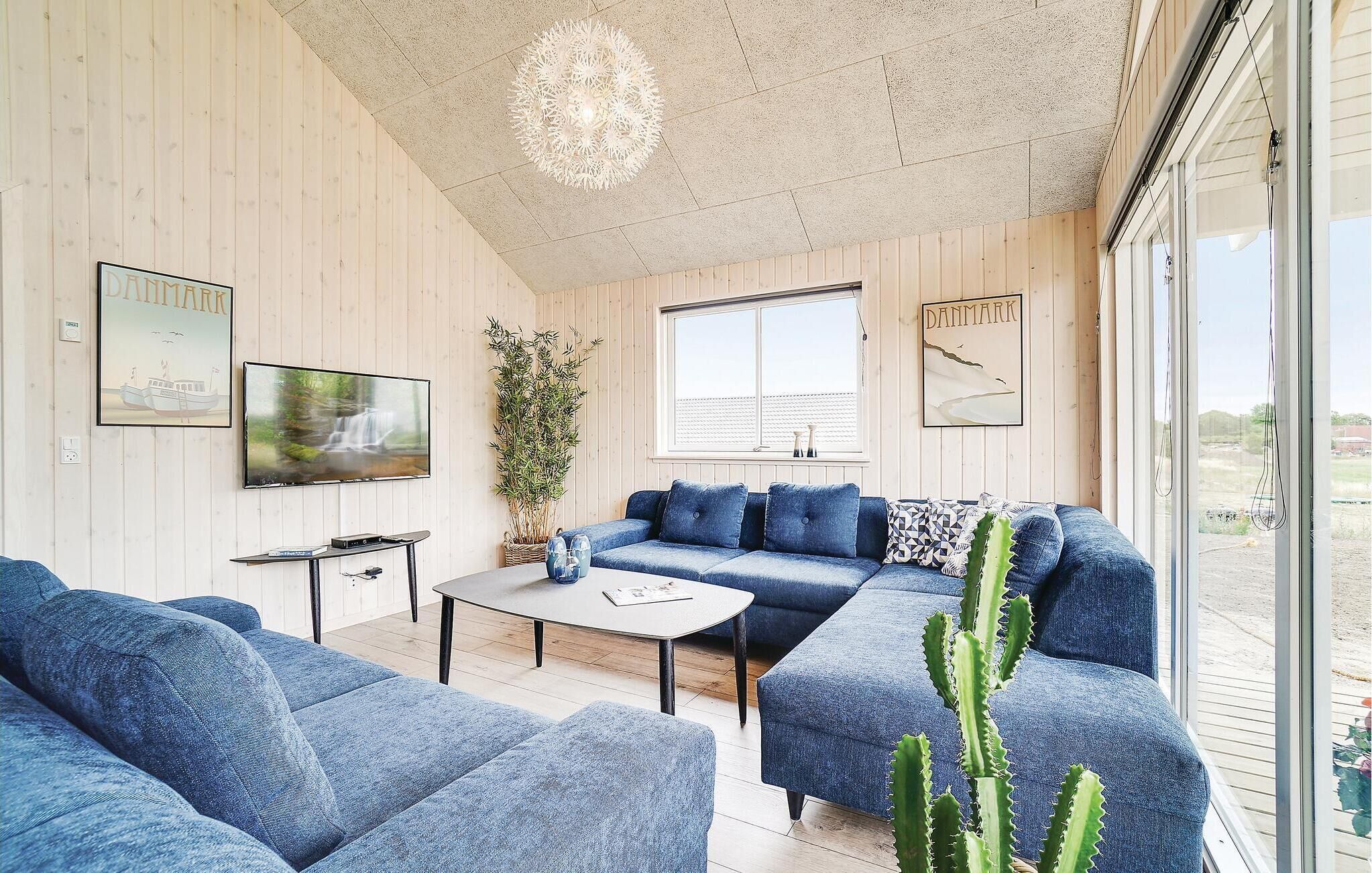 Een moderne woonkamer met een blauwe zithoek, een flatscreen televisie en een groot raam met uitzicht op het landschap.