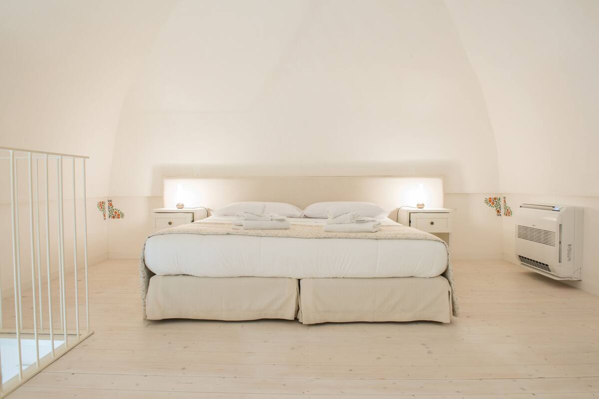 A bedroom with a large bed, bedside tables, and an air conditioning unit.