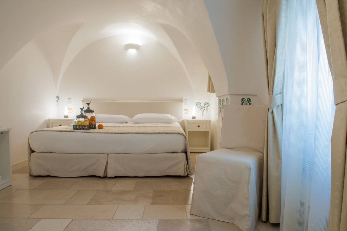 A spacious bedroom with a large bed, bedside tables, a nightstand, and a chair.