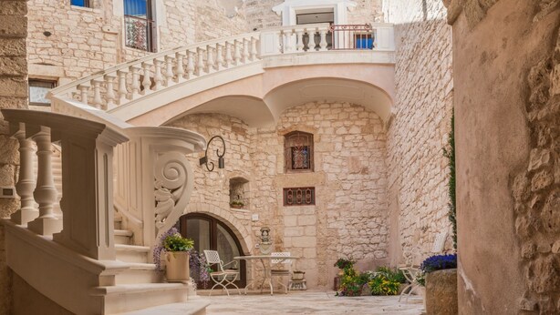 A stone courtyard with a staircase, a balcony, and a table with chairs. - Dimora dell'Osanna (Carovigno)