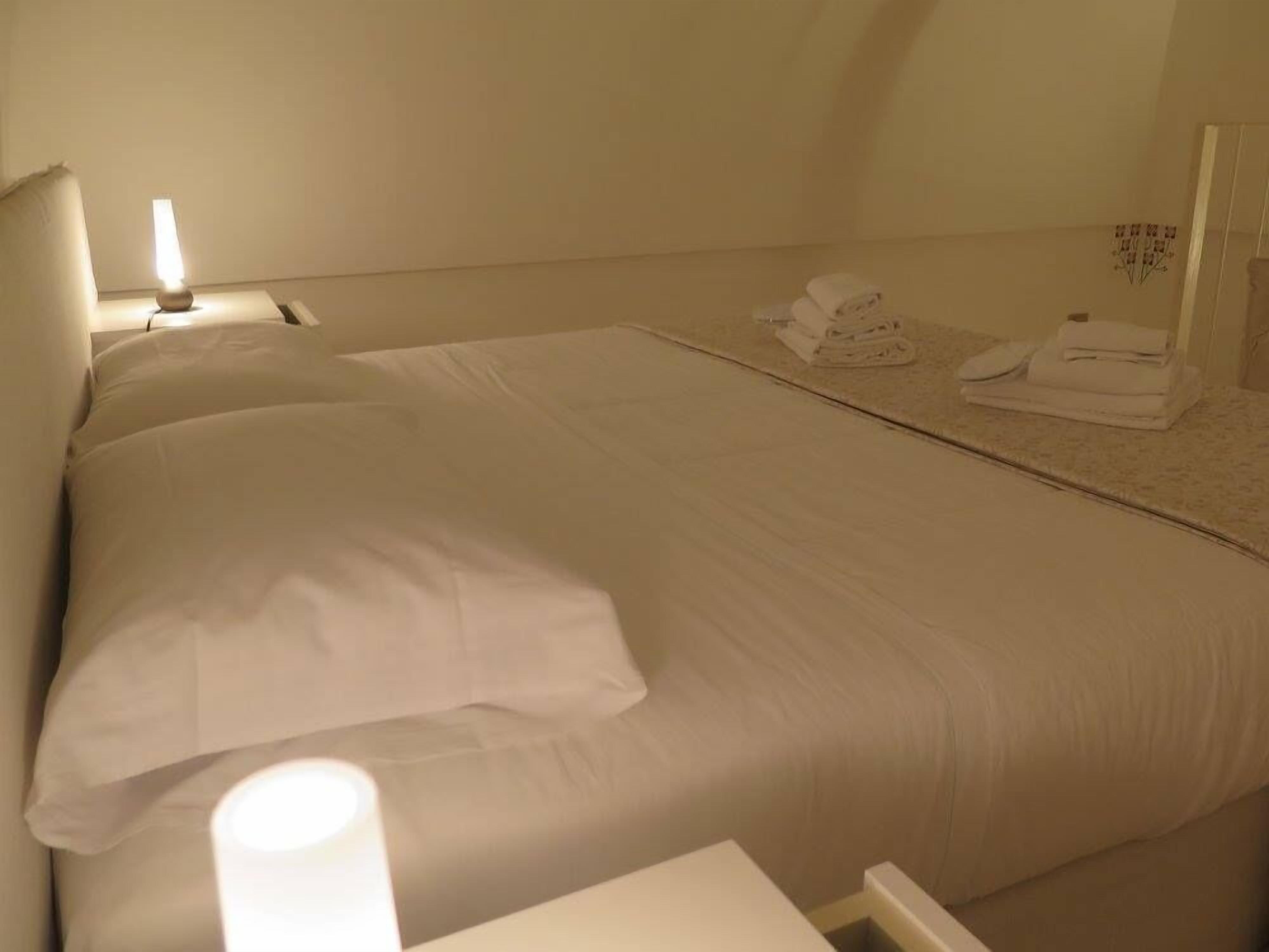 A hotel room with a large bed, a bedside lamp, and neatly folded towels on the floor.