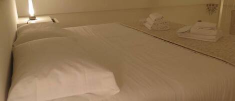 A hotel room with a large bed, a bedside lamp, and neatly folded towels on the floor.
