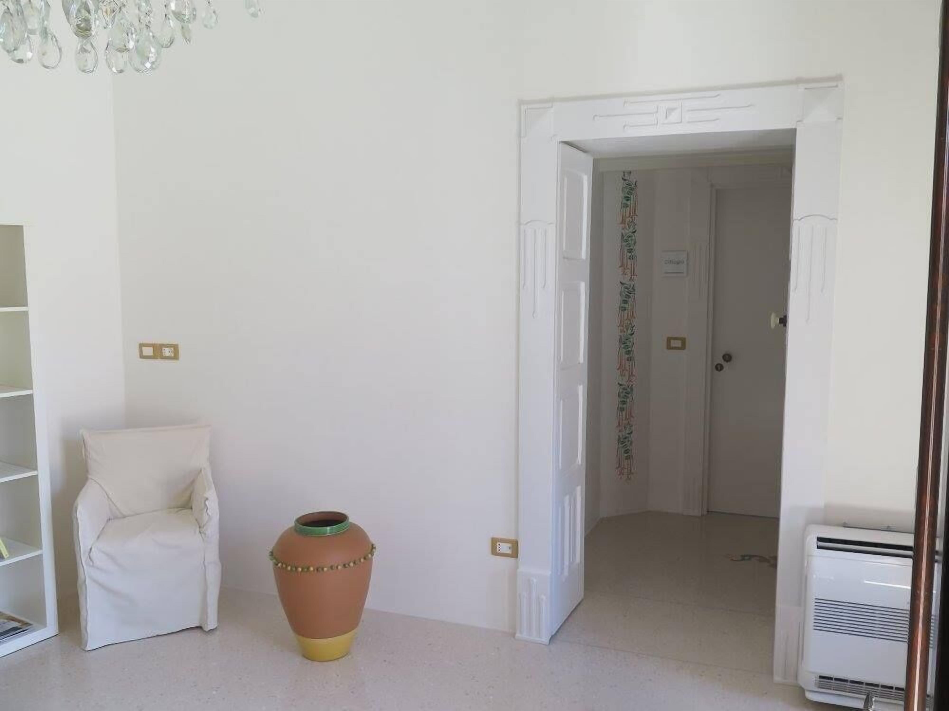 A room with a white chair, a terracotta pot, a white door, and an air conditioning unit.