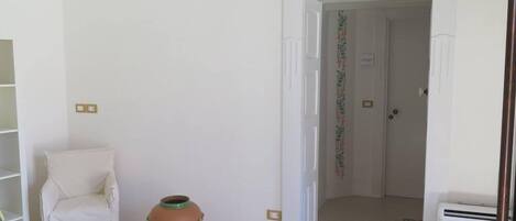 A room with a white chair, a terracotta pot, a white door, and an air conditioning unit.