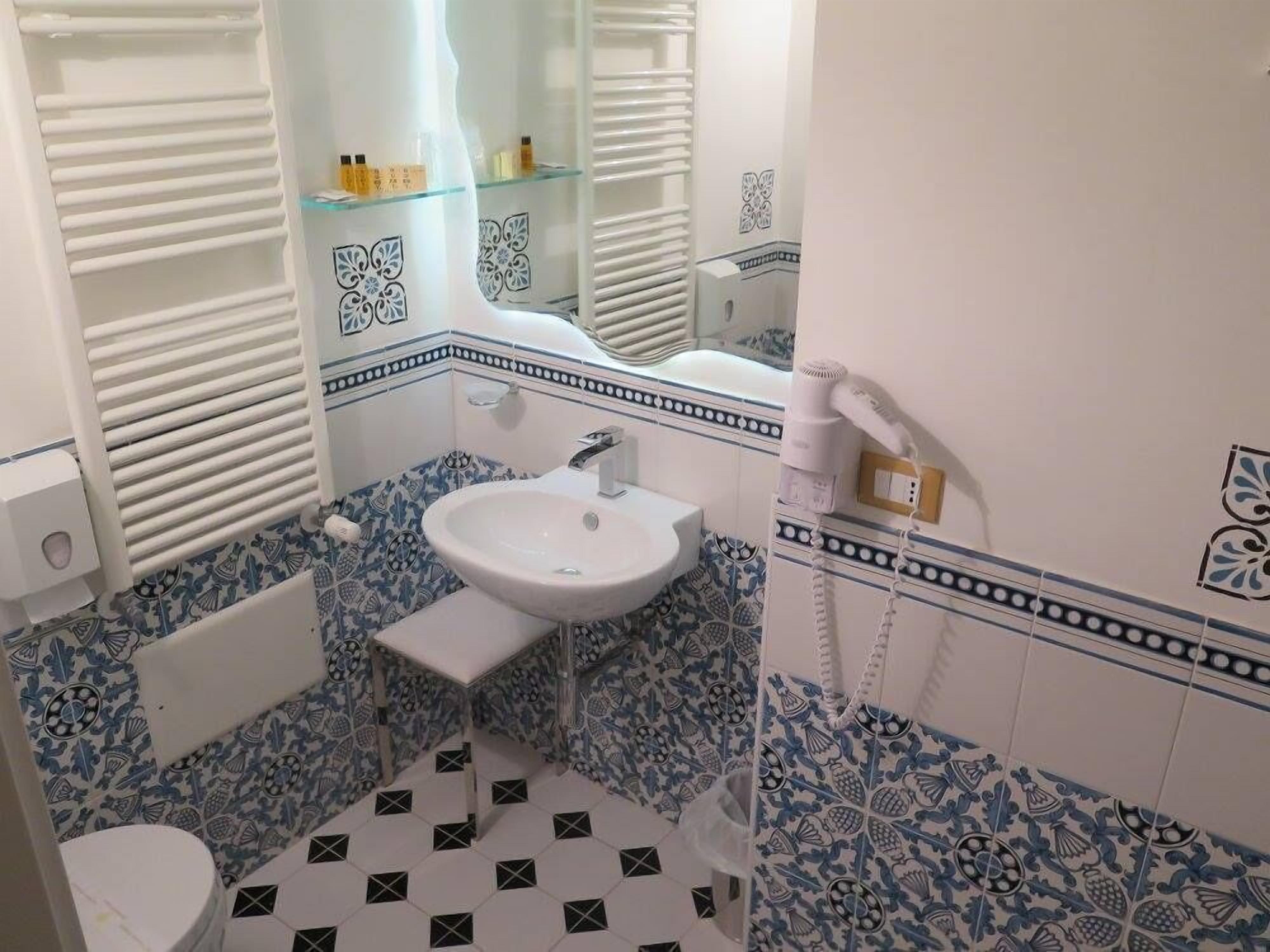 A bathroom with a white sink, a mirror, a handheld showerhead, and a toilet.