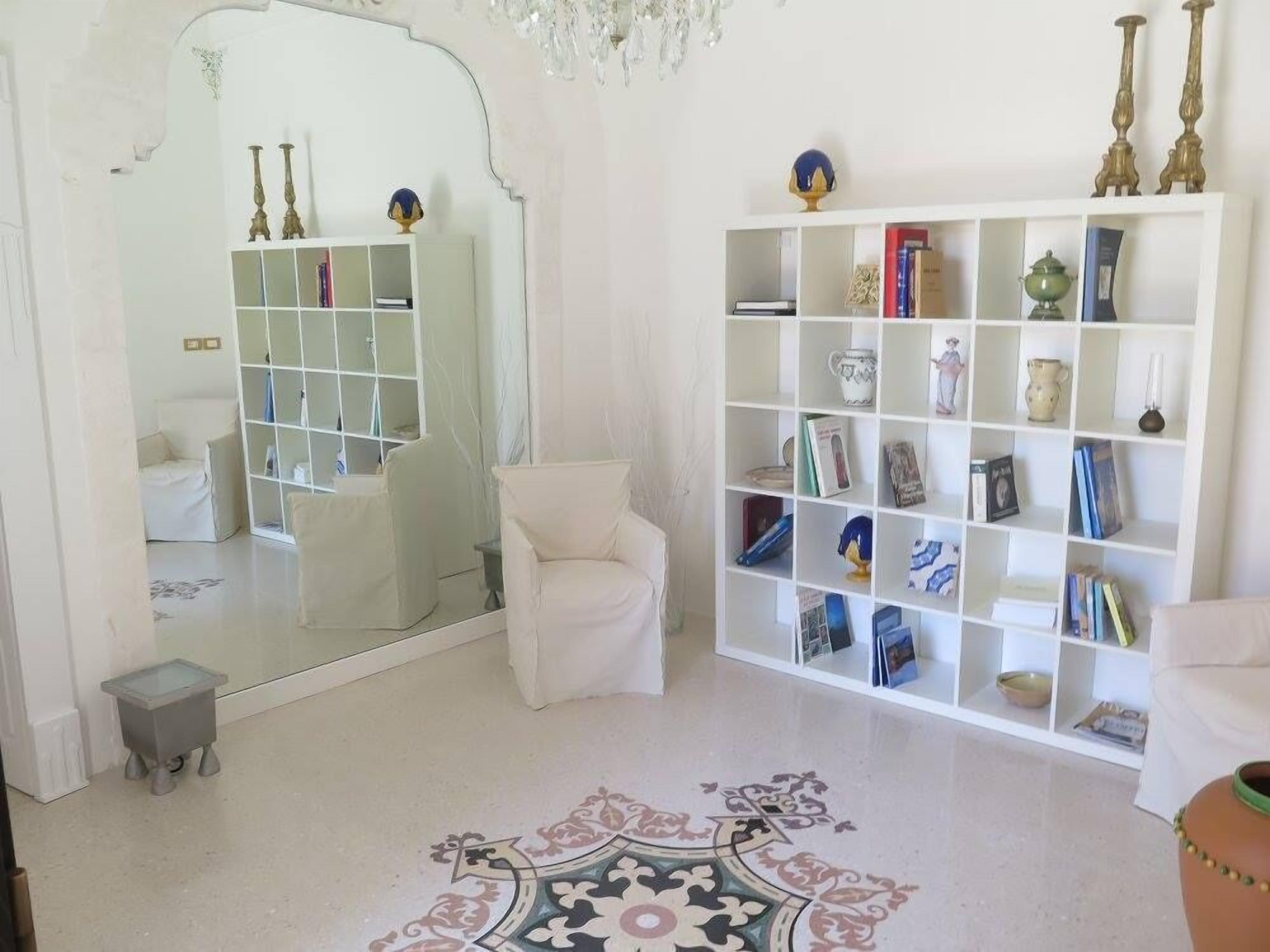 A modern living room with a white sofa, a mirrored wall, a white bookshelf, and a patterned rug.