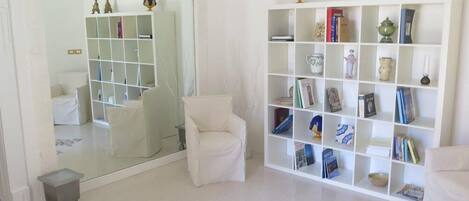 A modern living room with a white sofa, a mirrored wall, a white bookshelf, and a patterned rug.