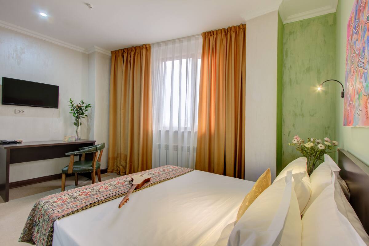 Une chambre d’hôtel avec un lit, un bureau, une chaise, une télévision et un tableau au mur.