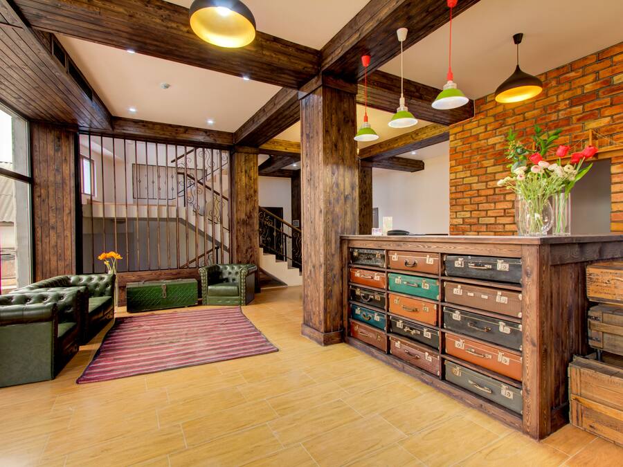 Un vestíbulo amplio con una escalera de madera, sofás de cuero, un tapete estampado y una pared decorada con maletas antiguas.