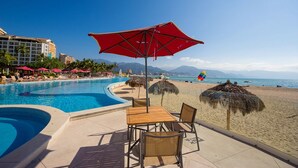 A resort pool area with a red umbrella, lounge chairs, and a view of the beach and ocean.