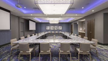 A conference room with a long table, chairs, a projector, and a screen.
