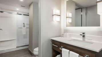 A modern bathroom with a glass shower enclosure, a white sink with a mirror, and wooden cabinets.