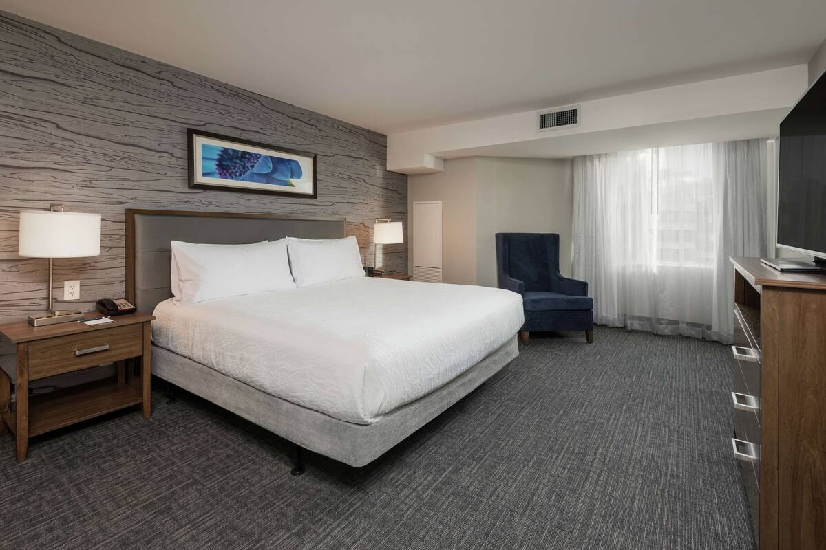 Une chambre d’hôtel avec un grand lit, un bureau avec une lampe, une chaise et un téléviseur.