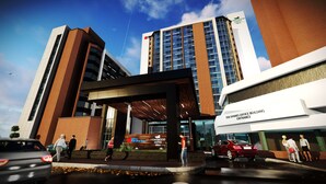 Een moderne hotelingang met een opvallend bord voor Homewood Suites Hilton, een overdekte doorgang en een rode auto die er geparkeerd staat.