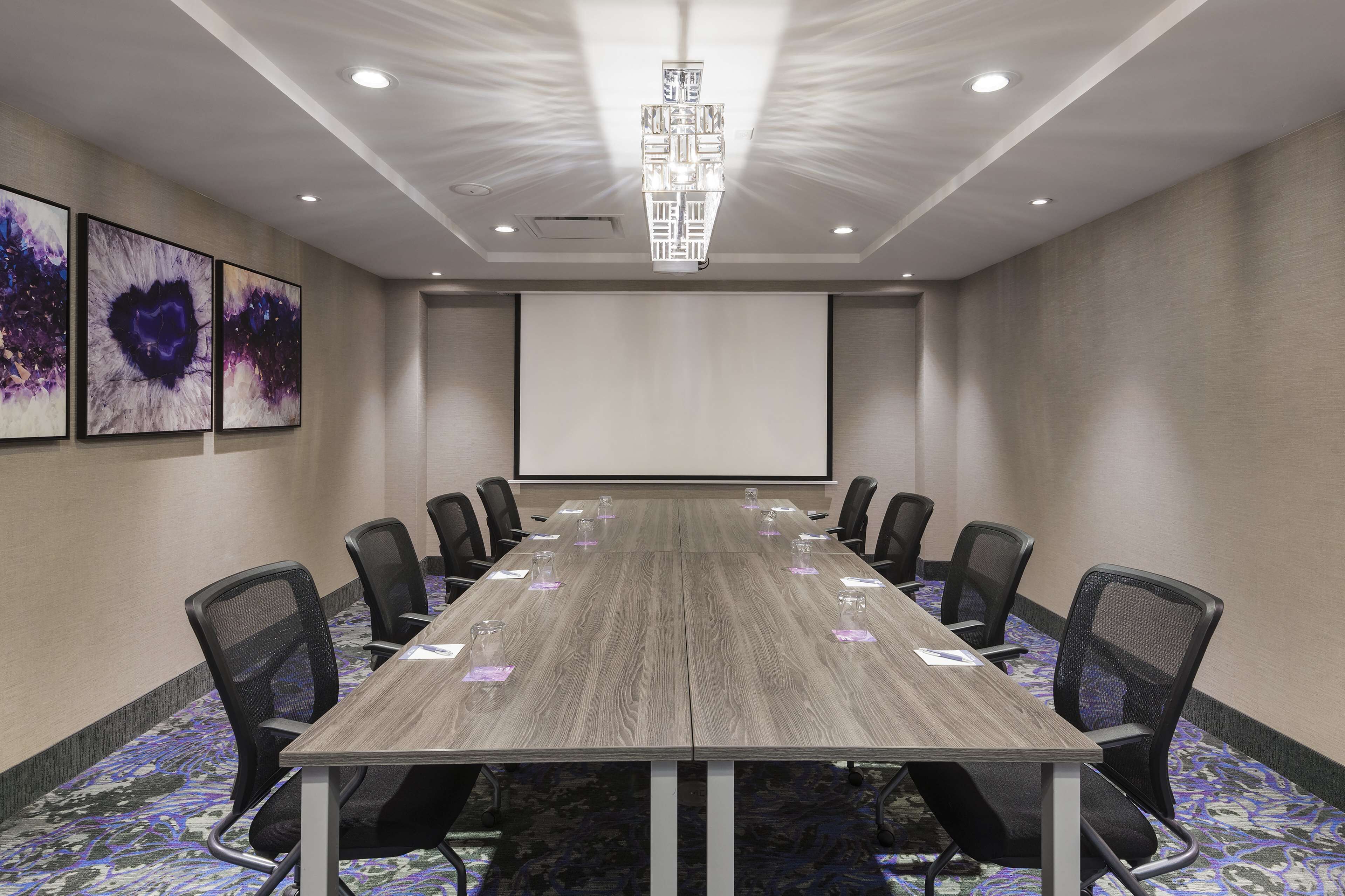A conference room with a long table, black chairs, and a projector screen.