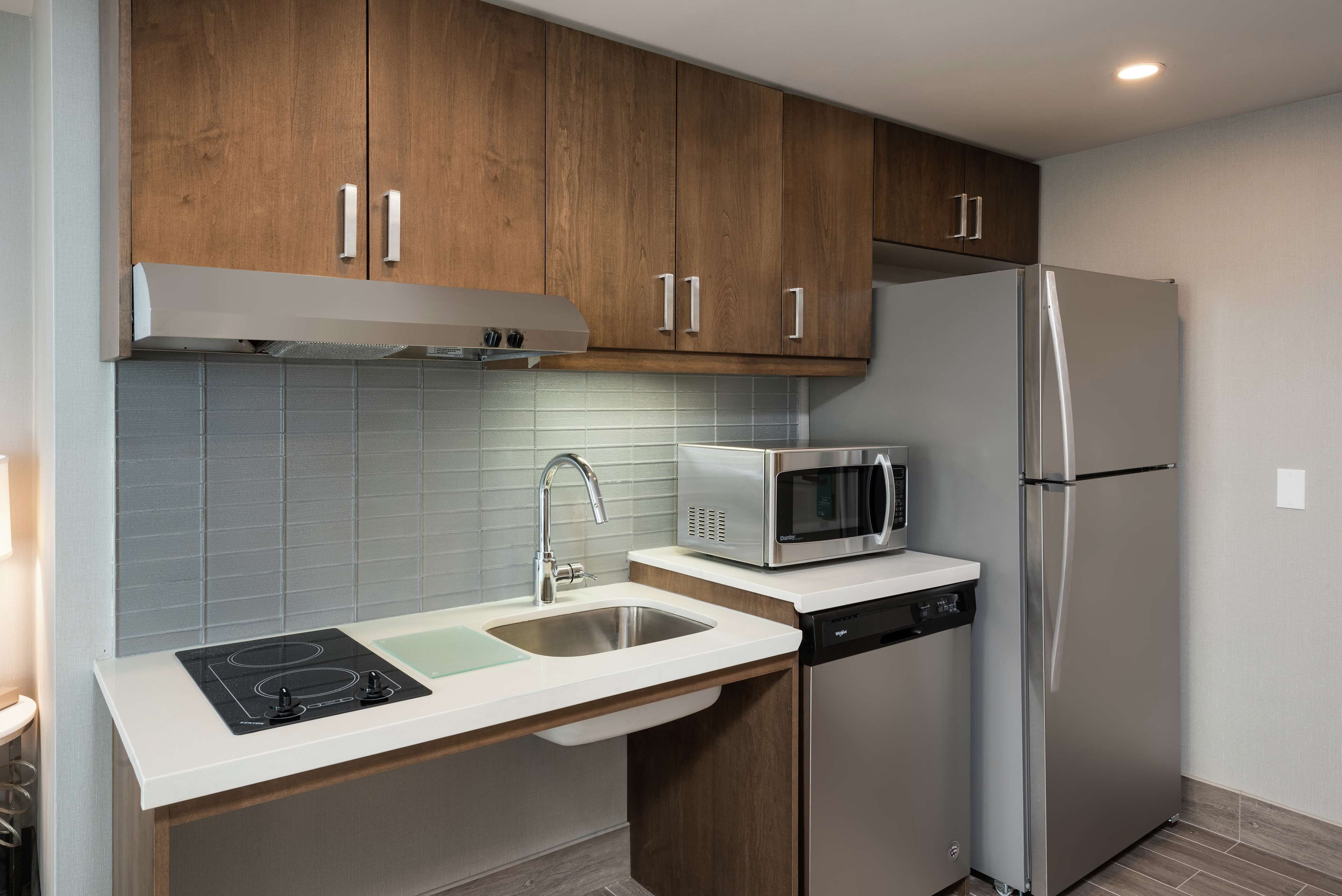 A compact kitchen with wooden cabinets, a stainless steel refrigerator, a microwave, and a dishwasher.
