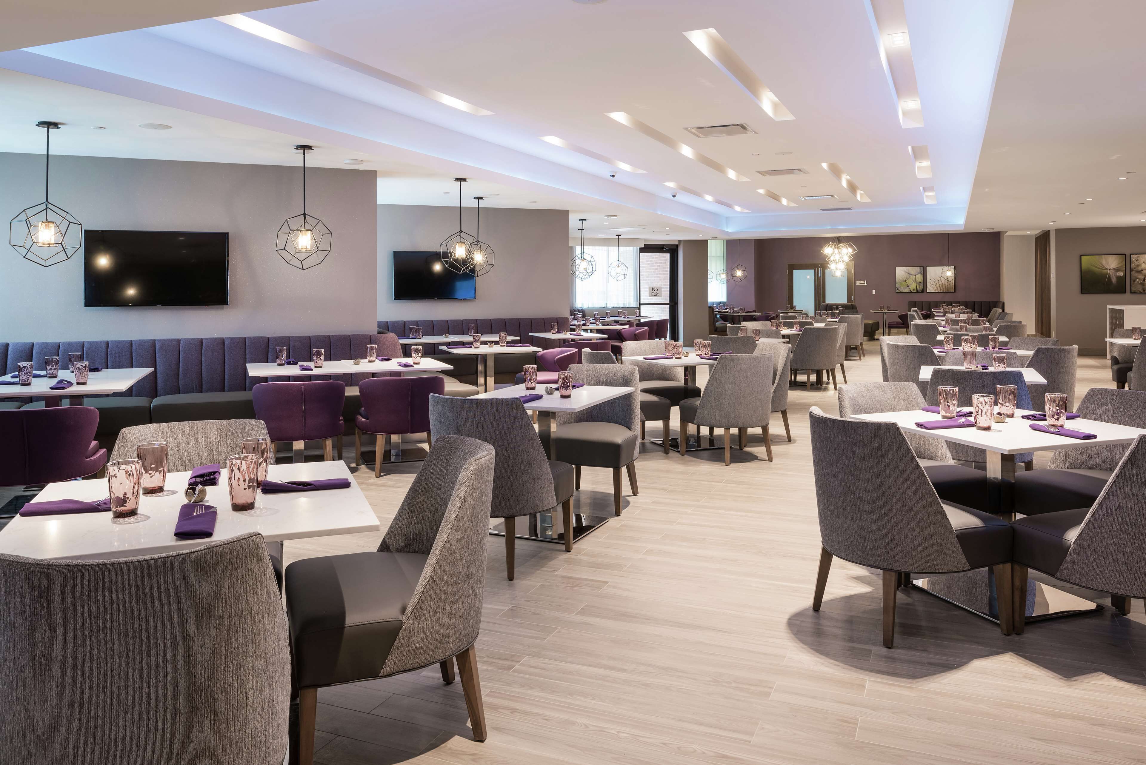 A modern restaurant with multiple dining areas, including booths and tables, and a large flat-screen TV mounted on the wall.